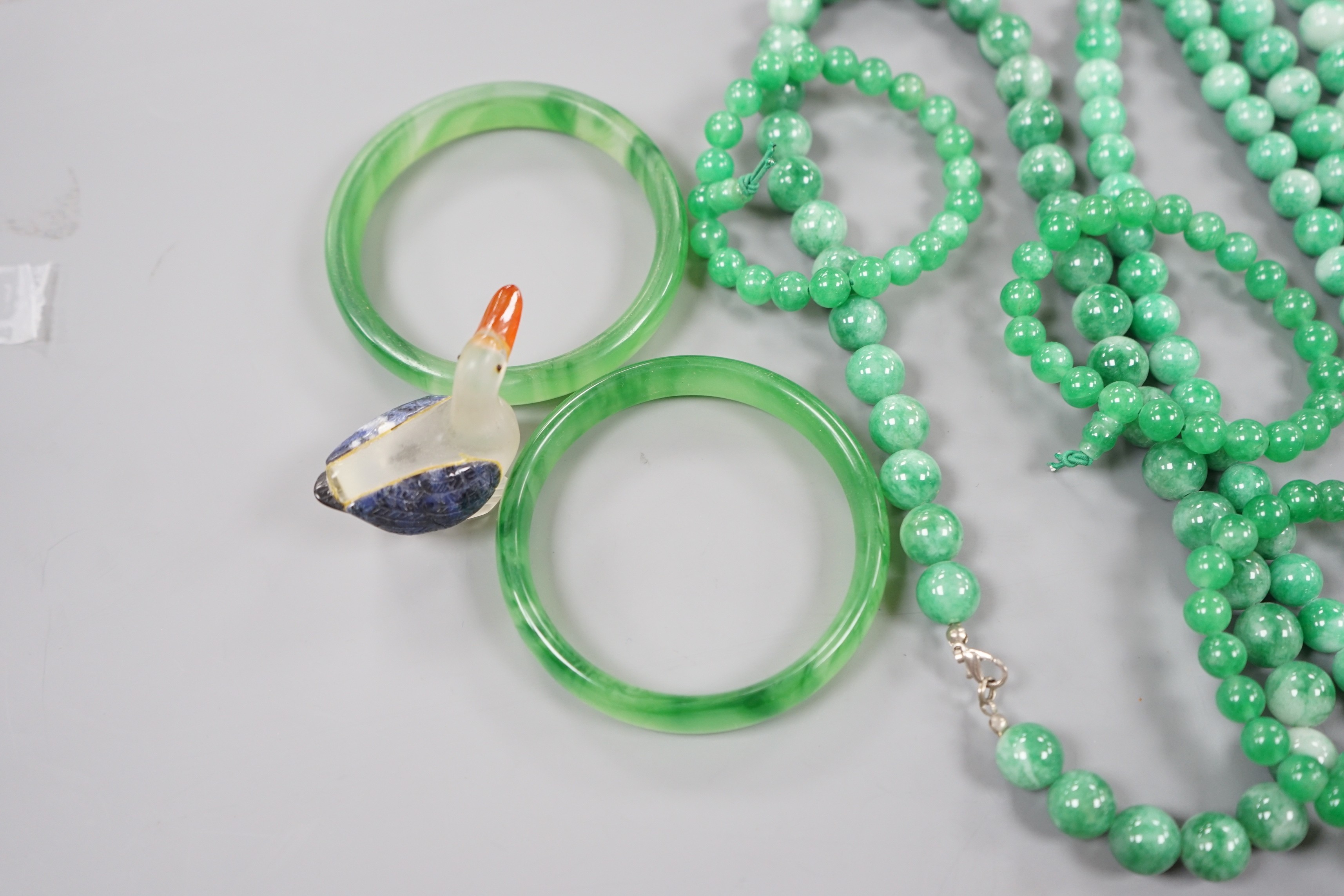 A group of three jadeite necklaces, together with two jadeite bracelets, two green glass bangles and a glass figure of a duck (8)